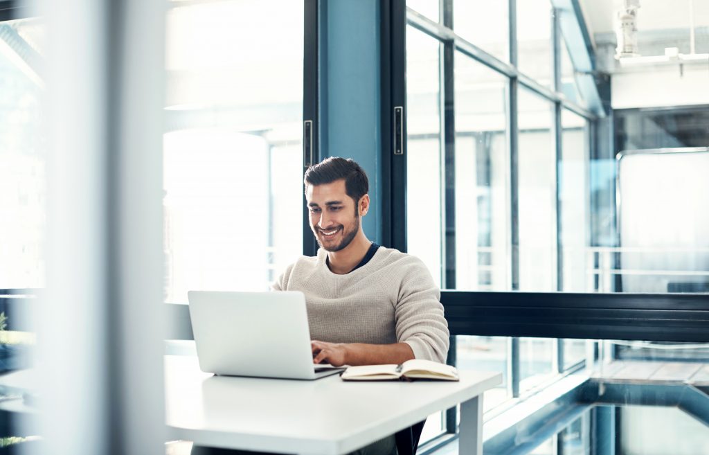 Shot of a young businessman using a laptop at his desk in a modern office
